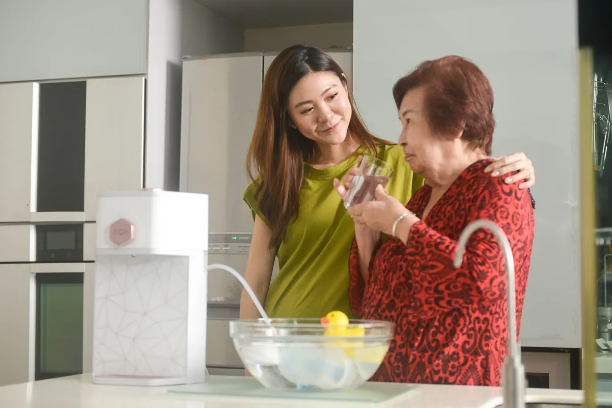 A woman with her arm around her mother as she drinks a glass of AOX water in their kitchen