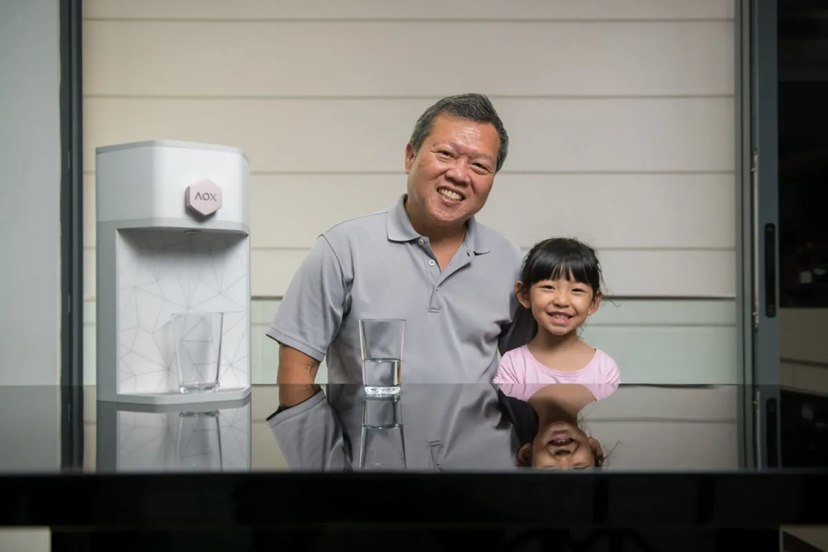 A smiling grandfather with his granddaughter at home beside their AOX dispenser