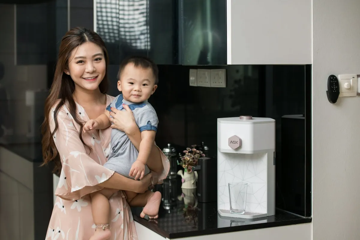 A smiling mother holding her baby son in their new kitchen beside their AOX dispenser
