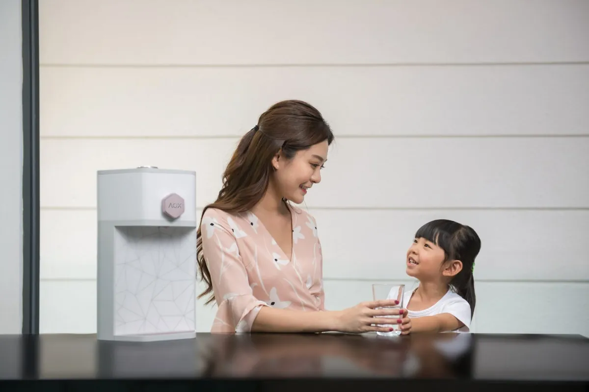 A mother smiling as she hands her young daughter a glass of water beside their AOX dispenser