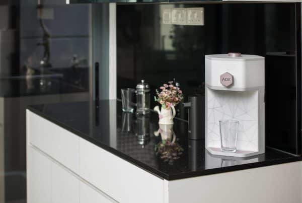 AOX Compac O2+ water dispenser elegantly placed in a modern kitchen with a glass and floral decor.