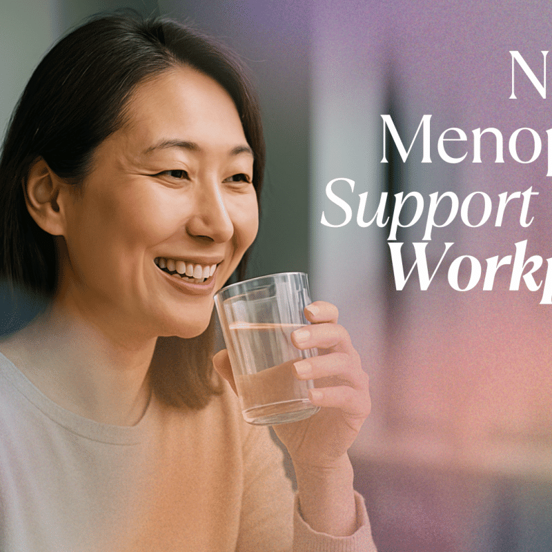 Middle-aged Asian woman smiling while drinking water in a bright office setting, representing natural menopause support in the workplace.